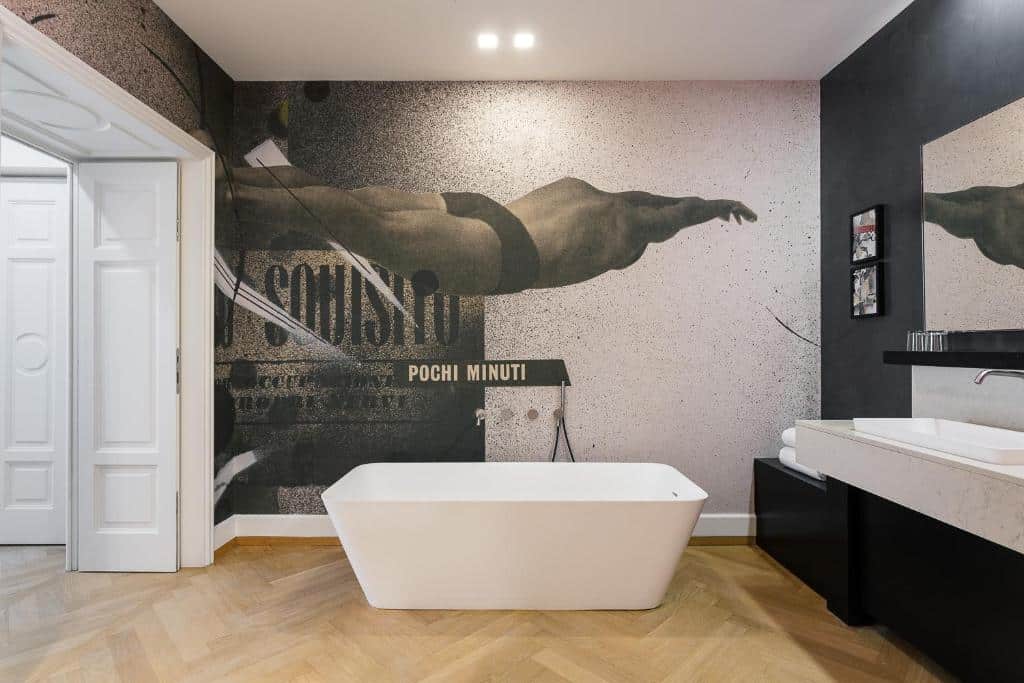 Banheiro amplo do Galleria Vik Milano com uma banheira de hidromassagem, chão que imita madeira e um móvel com toalhas brancas, para representar hotéis de luxo em Milão