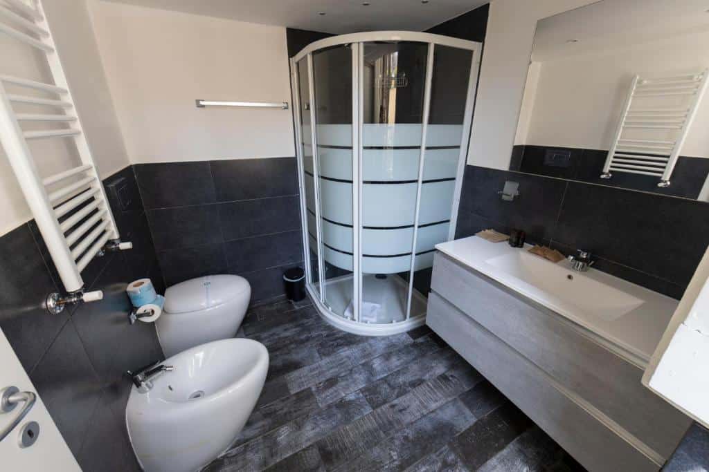 banheiro do Arch Rome Suites, com vaso e bidê, pia comprida com duas torneiras e um box de vidro que parece um elevador