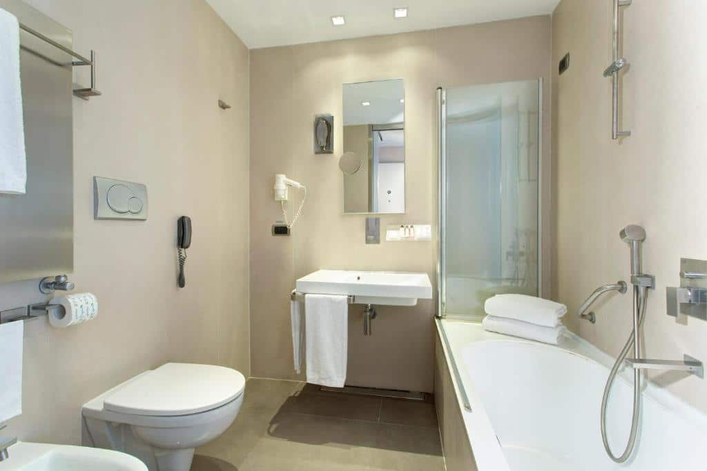 banheiro do Best Western Premier Hotel Royal Santina com adaptaçõe, como pia mais baixa com espaço para cadeira de rodas, vaso sanitário mais alto, bidê, banheira com barras de apoio e chuveirinho