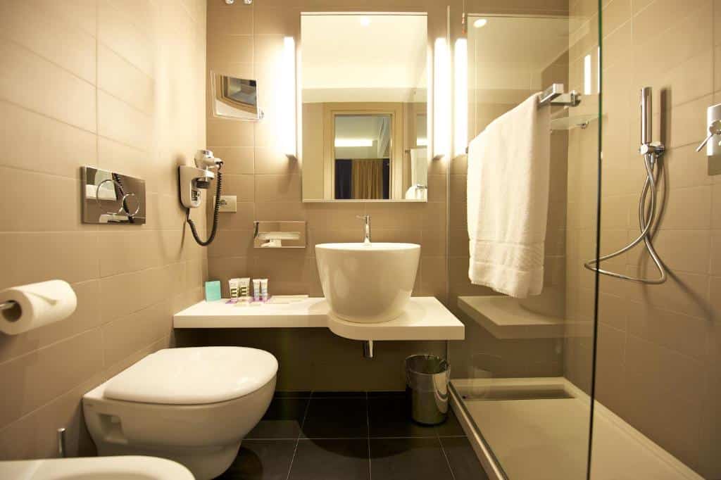 banheiro do Mercure Roma Centro Colosseo com cadeira de banho, pia mais baixa e vaso elevado em louça arredondada, há chuveirinho e bidê