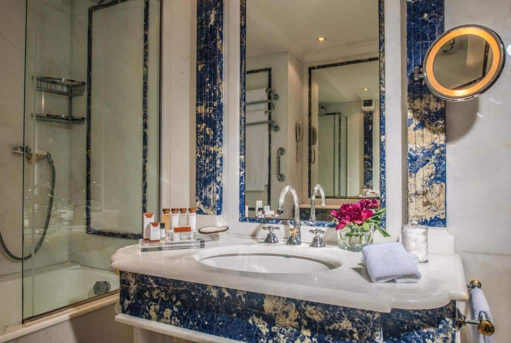 banheiro com adaptações para pcds com pia com espaço embaixo, detalhes em mármore azul, banheira com chuveirinho e muitas barras de apoio