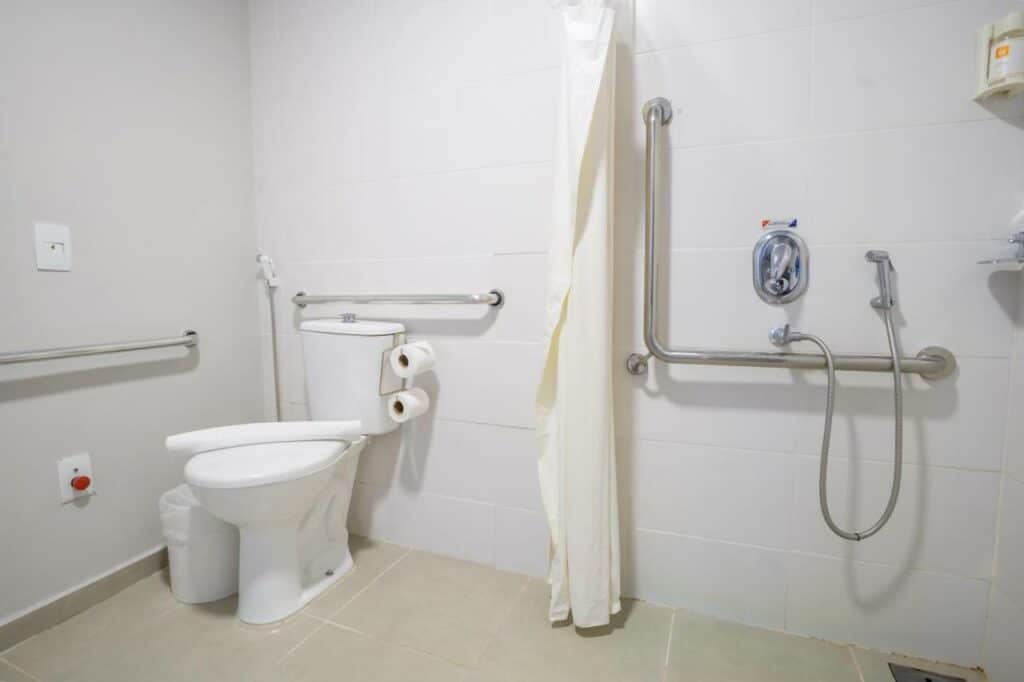 Banheiro com vaso sanitário, área do chuveiro e várias barras de apoio. Foto para ilustrar post sobre hotéis em Campo Grande.