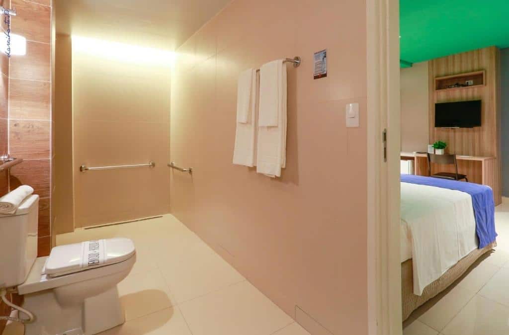 Banheiro de hotel com paredes beje, toalhas brancas, privada e barras de apoio para acessibilidade. Imagem para ilustrar o post hotéis em Teresina.