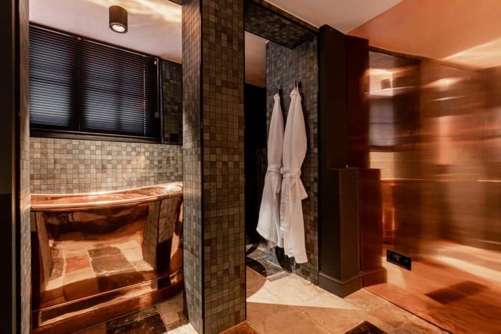 Banheiro de um dos quartos do Hotel The Craftsmen, com uma banheira cromada e dois roupões pendurados na parede