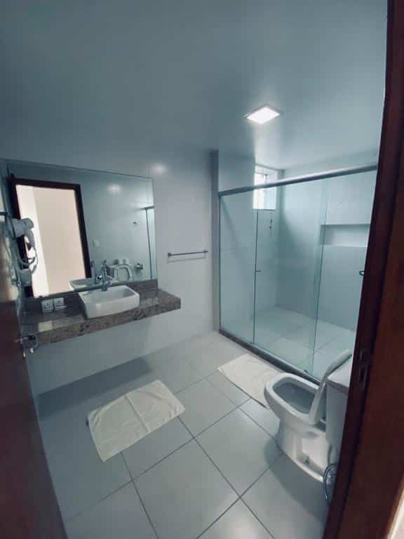 Banheiro de hotel bem espaçoso com pia, espelho, box bem largo e privada. Imagem para ilustrar o post hotéis em Cabo Frio.