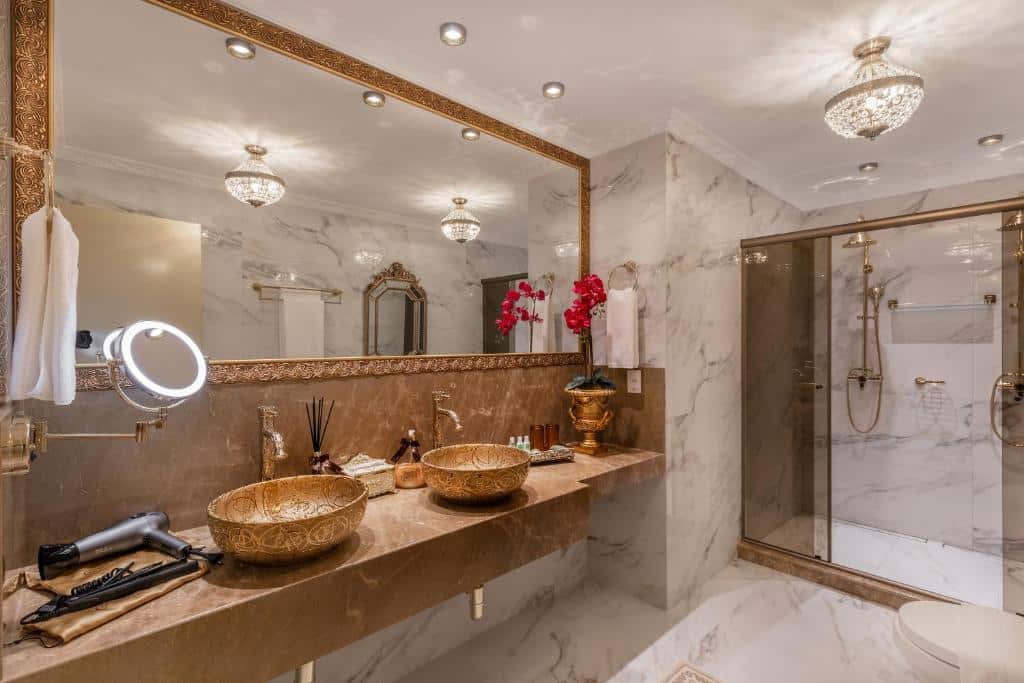 banheiro revestido em mármore com pia dupla, cubas douradas, espelho amplo e box com detalhes em ouro velho.