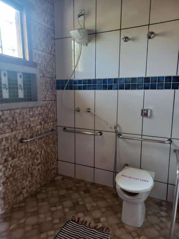 área do banheiro da pousada cachoeiras do cipó mostrando o chuveiro e o vaso sanitário com diversas barras de apoio nas paredes