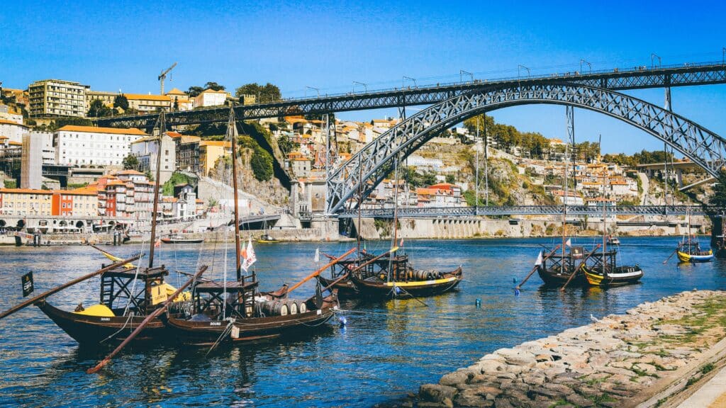 Rio Douro no Porto, Portugal durante o dia com barcos no rio e ao fundo uma ponte e casas.