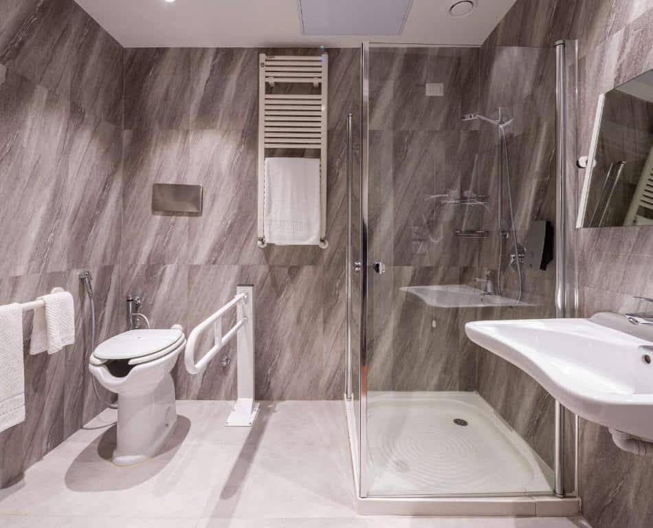 Banheiro adaptado do Best Western Air Hotel Linate com barras de apoio, pia mais baixa e sem móvel embaixo, além de um box de vidro, para representar hotéis perto do aeroporto de Milão