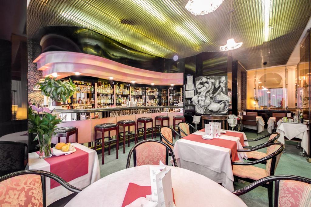 Área de refeições do Brunelleschi Hotel com um bar ao lado com bancadas acolchoadas, há diversas mesas quadradas e cadeiras, há alguns itens de decoração e lustres