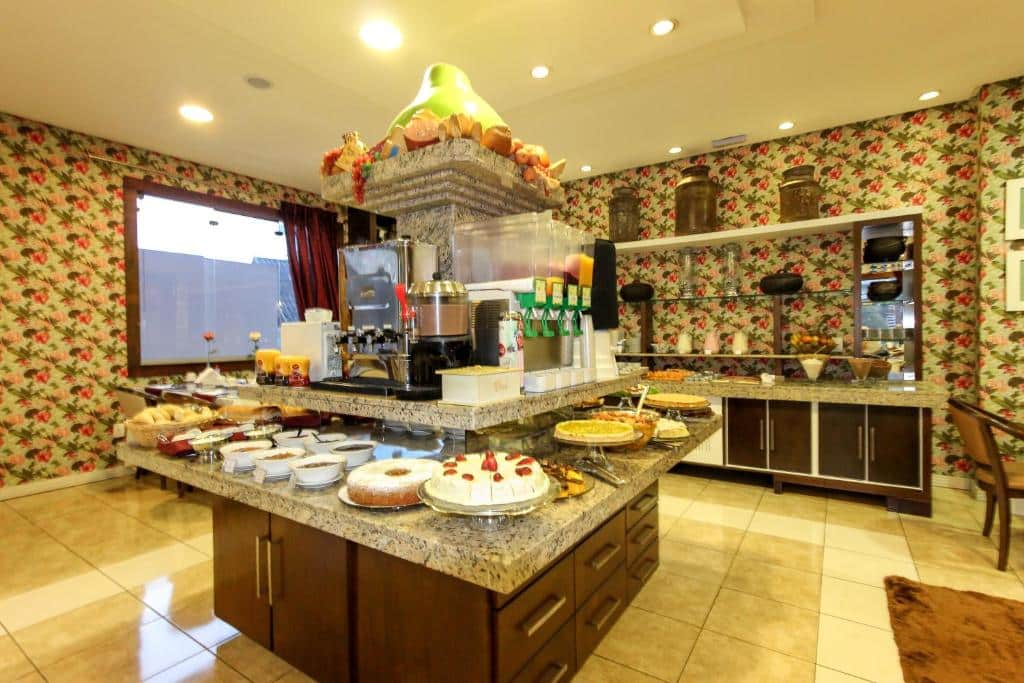 ilha do balcão de café da manhã do hotel glamour da serra com vários bolos, tortas doces e salgadas, bebidas e frutas.