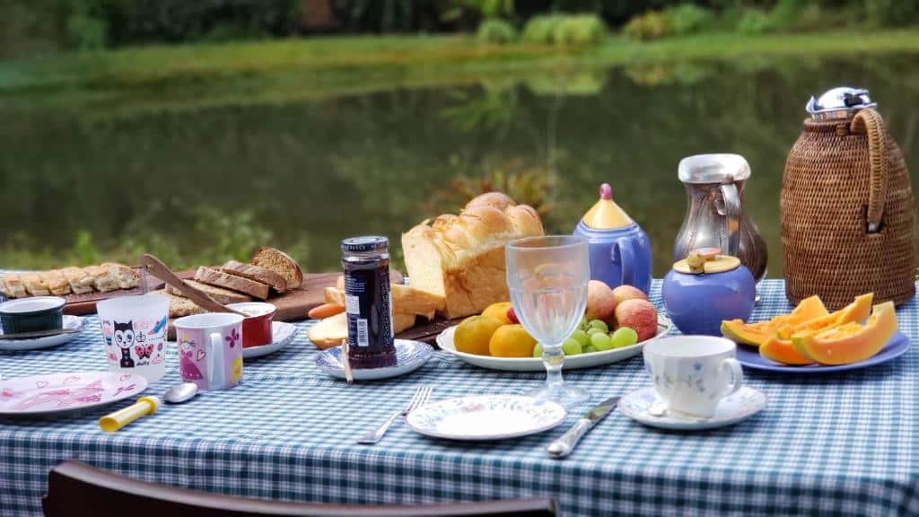 Uma mesa de café da manhã, com frutas e pães. Atrás um lago. Café da manhã do Villagio Serra da Cantareira. Foto para ilustrar post sobre Pousadas na Serra da Cantareira.