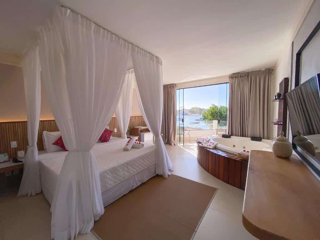 Quarto de hotel com cama de casal, banheira de hidromassagem e varanda com vista para o lago. Imagem para ilustrar o post hotéis em Cabo Frio.