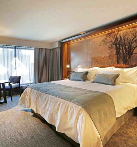 Quarto do Hotel Cumbres Lastarria com cama de casal do lado direito e do lado esquerdo uma mesa com cadeira. Representa onde ficar em Santiago.