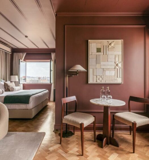 Quarto do Infante Sagres – Luxury Historic Hotel com cama de casal do lado esquerdo e do lado direito a frente duas cadeiras com uma mesa redonda. Representa hotéis de luxo no Porto.
