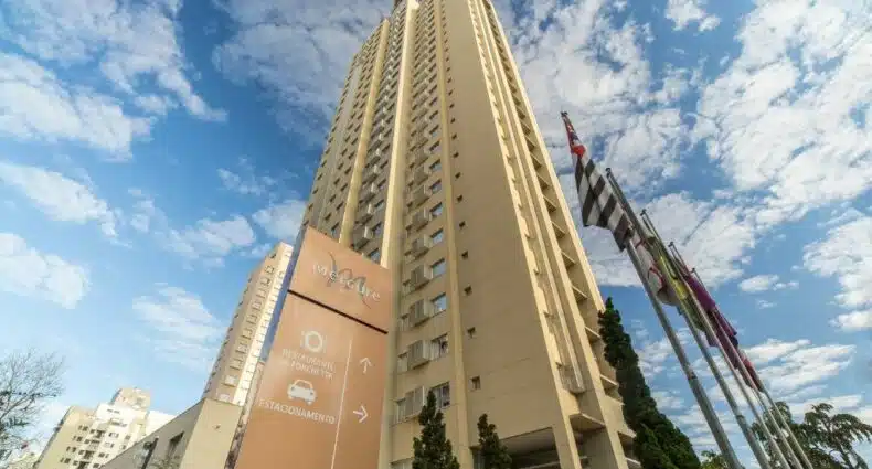 Hotel alto bege com uma placa marrom ao lado, algumas bandeira e árvores verdes durante o dia, ilustrando post Hotéis Mercure em São Paulo.
