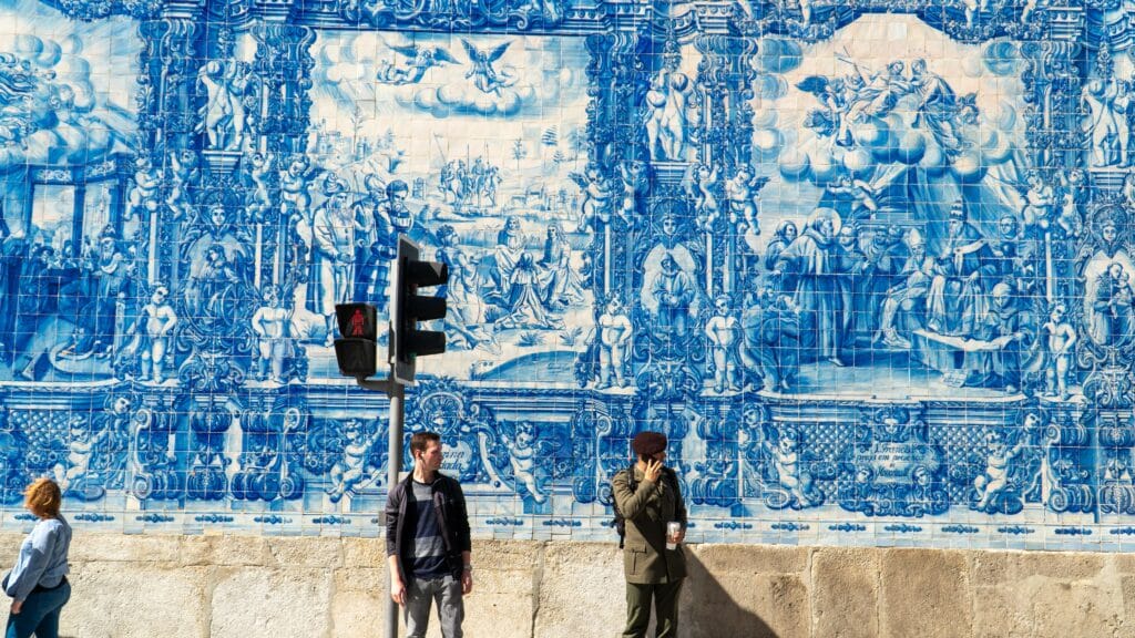 Capela de Santa Catarina e Senhora dos Anjos, com azulejos com esculturas santas durante o dia com dois homens parados no semáforo e uma mulher andando do lado esquerdo. Representa chip celular Porto