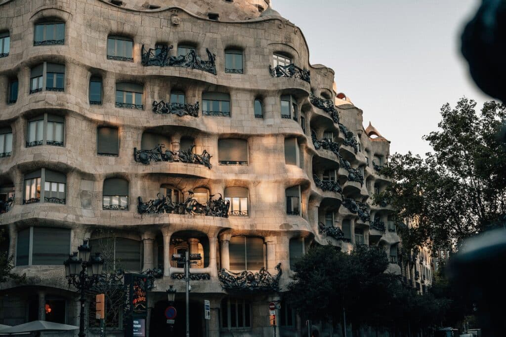 Fachada da Casa Milà. O local tem andares curvados como em movimento, e há várias árvores ao redor. - Foto: David Rüsseler via Unsplash