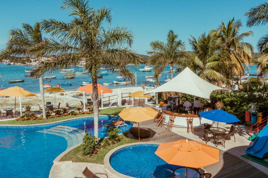 Hotel de frente para o mar com piscina, coqueiros, bar e mesas com guarda sol.
