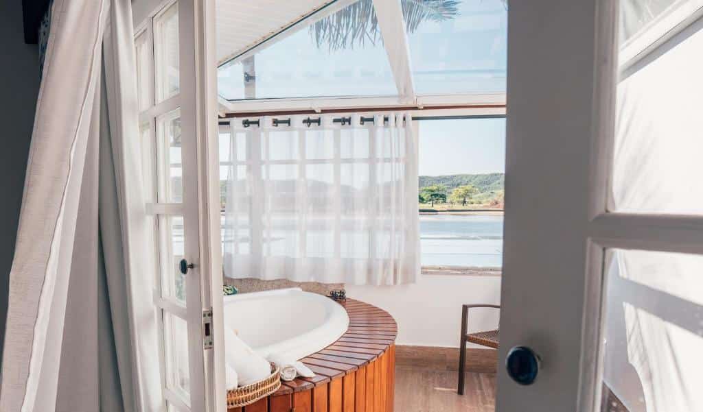 Varanda de hotel com cortinas brancas e banheira de hidromassagem com vista para o lago.
