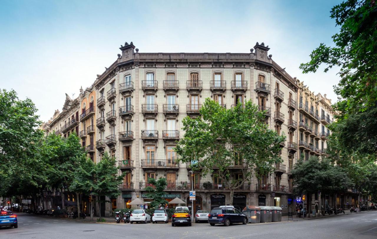 Fachada do Primavera Hostel, uma das recomendações de hostels em Barcelona. O belo prédio bege de cinco andares tem algumas árvores em frente, e carros estão estacionados ao redor do local.