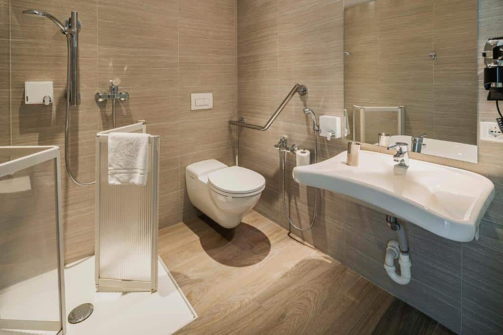 Banheiro adaptado do Fasthotel Linate com uma pia e espelho mais baixo, barras de apoio, box sem vidro e outros recursos