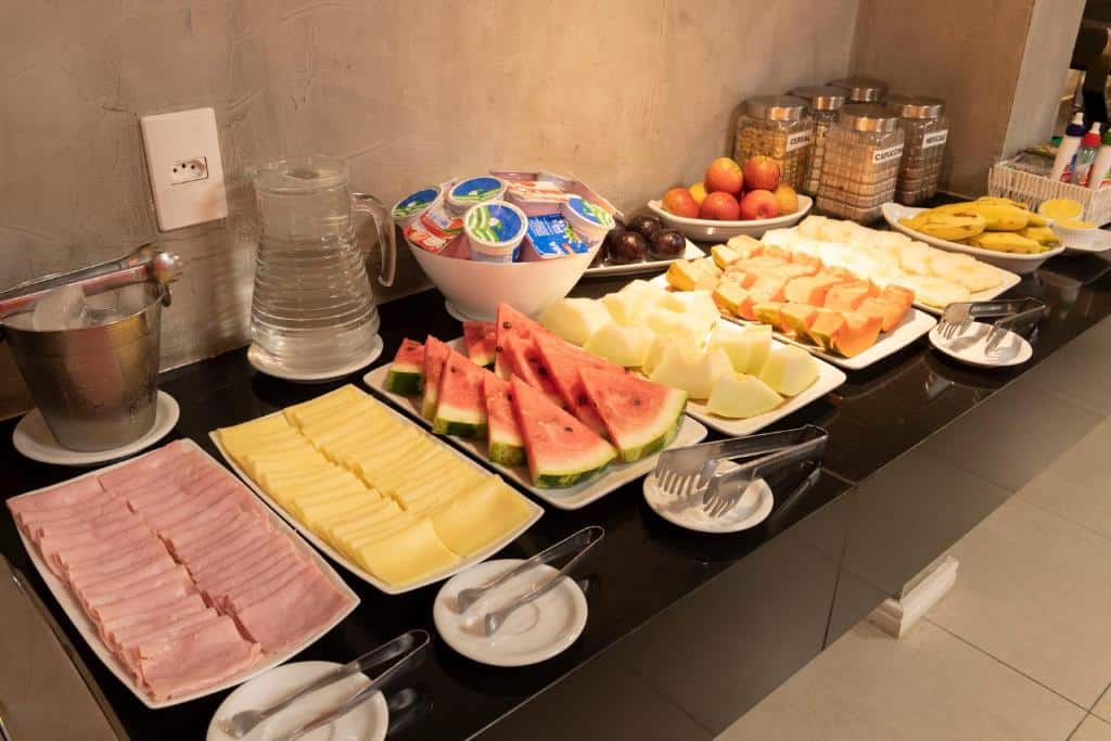 Bancada com café da manhã de um hotel em Teresina com frutas, frios, iogurtes e água.