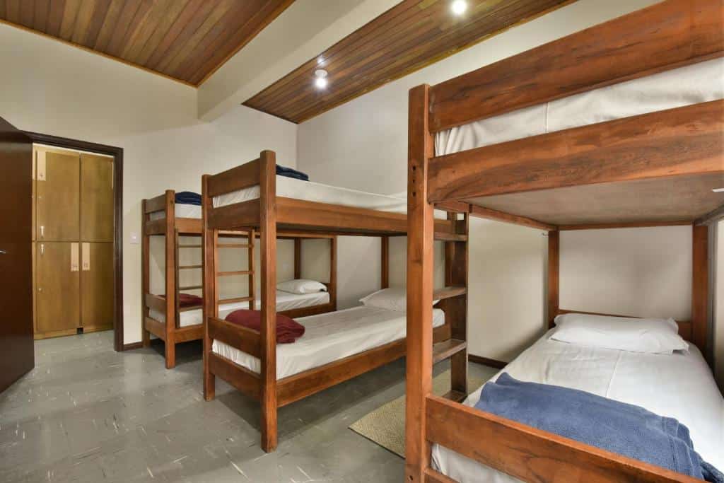 quarto compartilhado do hostel chocolatchê com três beliches de madeira, lençóis brancos e cobertores vermelhos e azuis em cada cama.