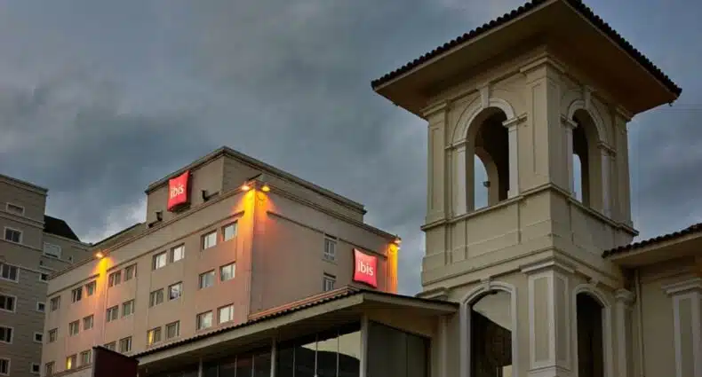 Parte da fachada do ibis Curitiba Batel, ao anoitecer de um dia com bastantes nuvens no céu, para ilustrar a capa do post "hotéis ibis em Curitiba"