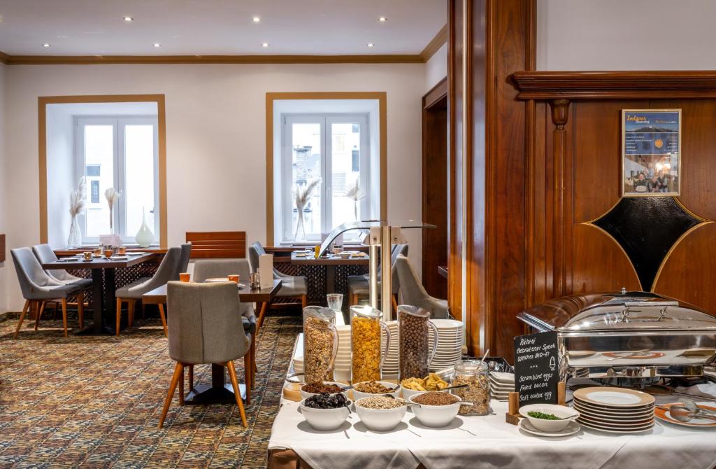 Parte da mesa com o café da manhã e atrás algumas mesas e cadeiras cinzas para fazer as refeições, ilustrando post Hotéis em Salzburg.