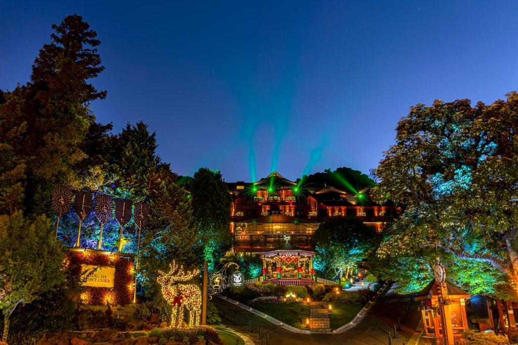 vista frontal e noturna do hotel casa daa montanha. O local possui muitas luzes coloridas e decorações de natal, tal como uma rena de pisca-pisca bem no jardim.
