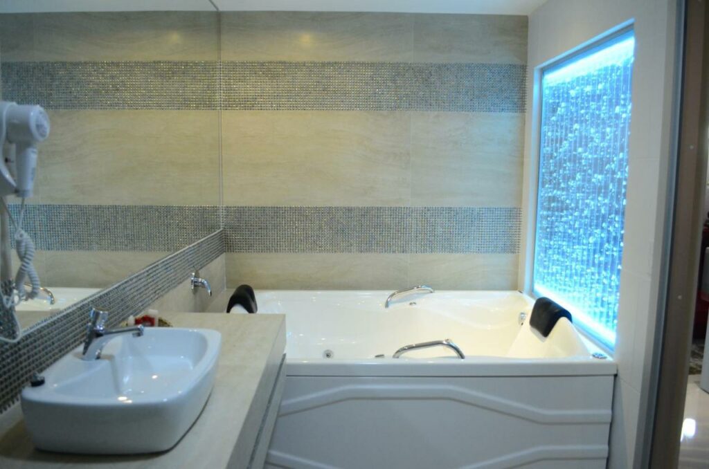 Banheiro do Hotel Girassol Plaza com banheira de hidromassagem, painel azul iluminado, pia, espelho e secador de cabelo.