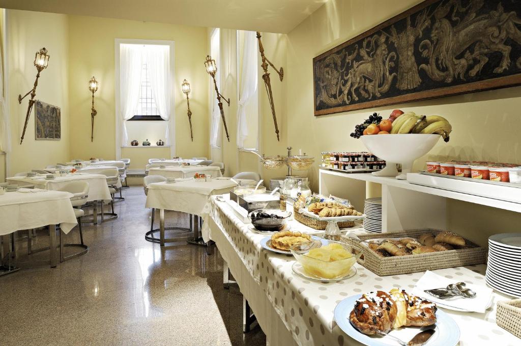 Área de refeições do Hotel Gran Duca Di York com mesas redondas e cadeiras estofadas, há uma mesa ampla com um café da manhã sendo servido