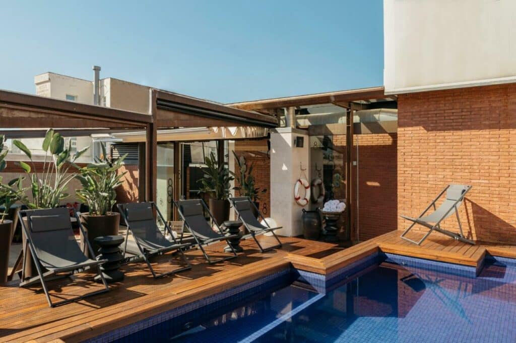 Área da piscina do Hotel Granados 83. Cadeiras de praia encaram a piscina e têm vasos de plantas por trás.