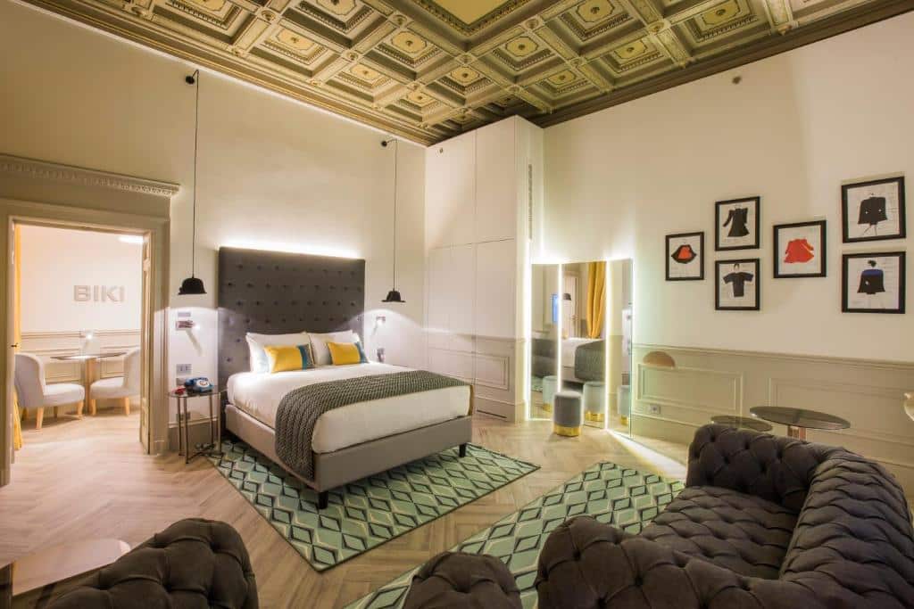 Quarto do Hotel Indigo Milan - Corso Monforte, an IHG Hotel bem espaçoso, com uma cama de casal, um armário branco, um espelho de corpo inteiro amplo, alguns quadros decorando o ambiente, um sofá com dois lugares e dois tapetes sob o chão que imita madeira