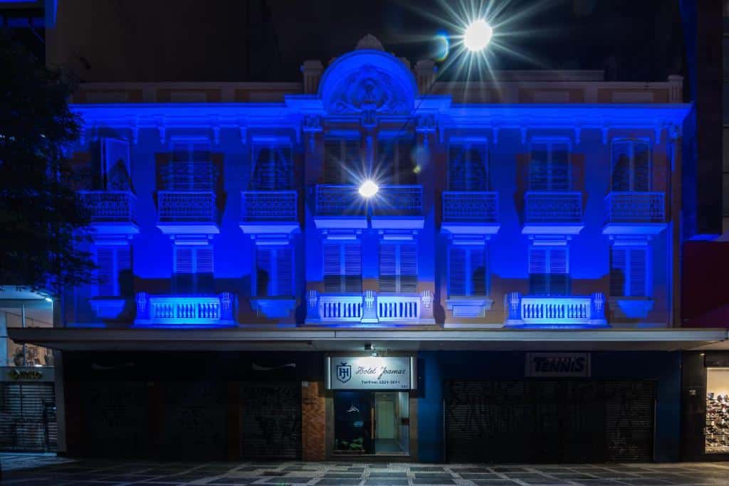 Fachada do hotel iluminado por uma luz azul, janelas branca e lojas a parte de baixo, ilustrando post Hotéis perto da 25 de Março em SP.