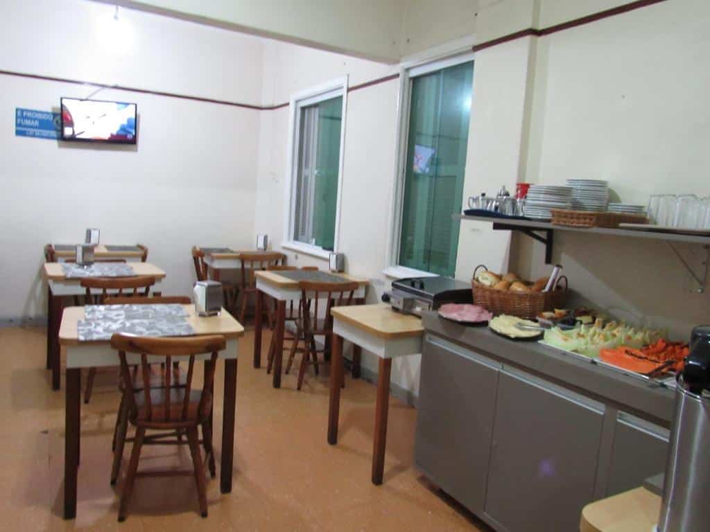 Parte do hotel com algumas mesas e cadeiras, comidas expostas, pratos e copos, e um tv na parede, ilustrando post Hotéis perto da 25 de Março em SP.