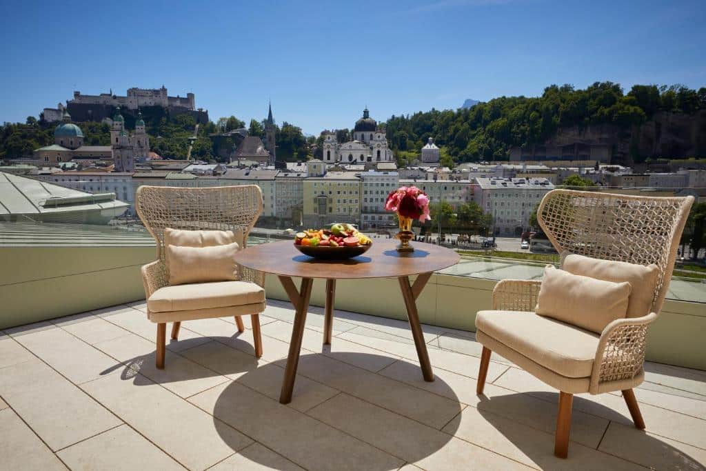 Duas poltronas e uma mesa no terraço do hotel com vista para a paisagem da cidade durante o dia, ilustrando post Hotéis em Salzburg.