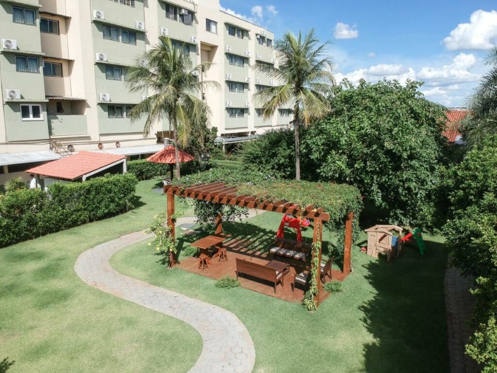Área verde com espaço para caminhada, árvores, brinquedos para crianças e um pergolado no meio, com bancos e cadeiras. Foto para ilustrar post sobre hotéis em Campo Grande.