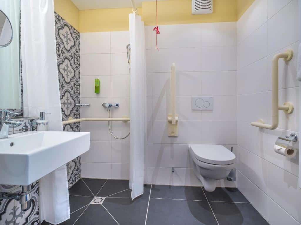 Banheiro do hotel mostrando a acessibilidade com barras de apoio perto da privada e perto do chuveiro.