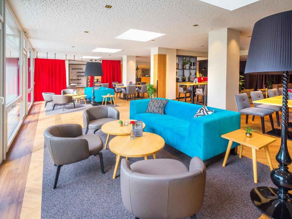 Parte do hotel para se reunir com as pessoas, com algumas poltronas cinzas, mesas de madeira e sofá azul em cima de tapete cinza, ilustrando post Hotéis em Salzburg.