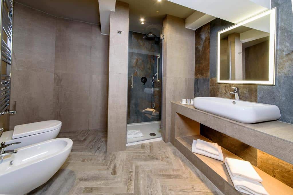 Banheiro espaçoso do Just Hotel Milano com um box de vidro, uma cuba ampla com uma pia, um espelho iluminado, toalhas disponíveis, além de um vaso sanitário e um bidê