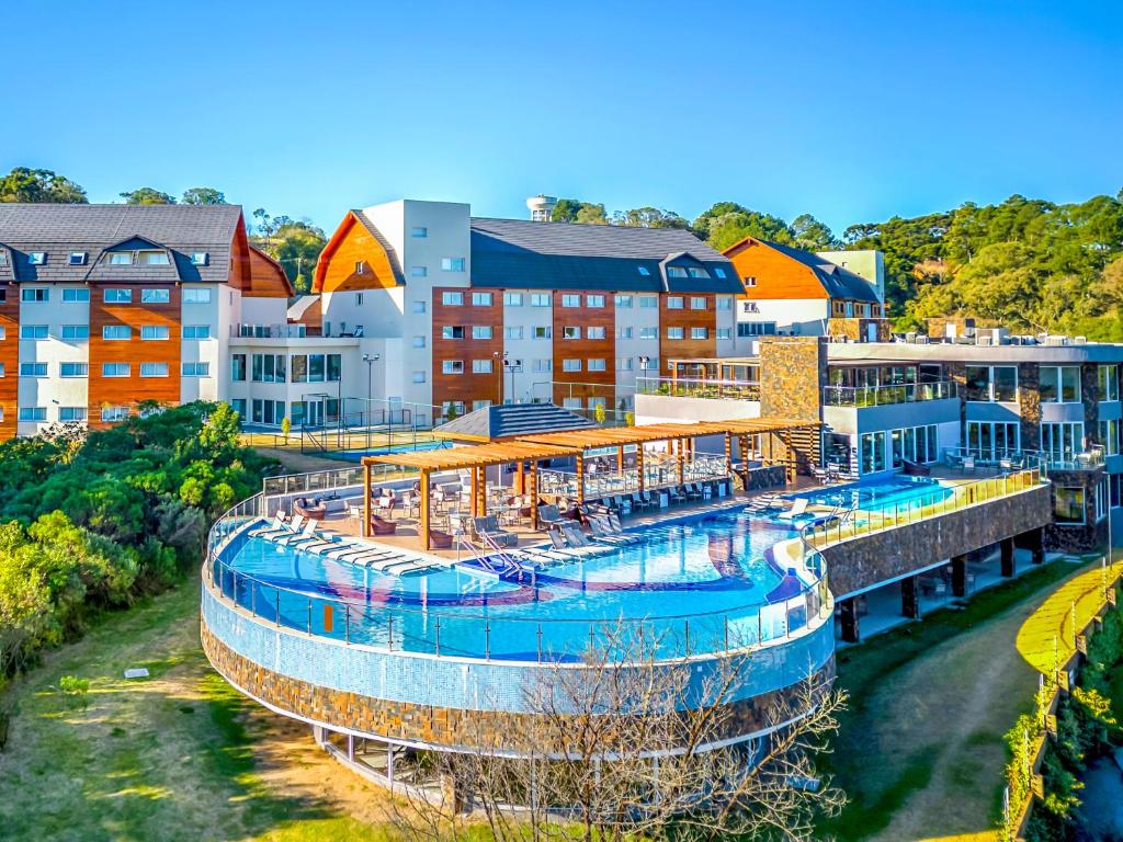 Vista do Laghetto Resort Golden Gramado mostrando a piscina com uma área coberta, repleta de espreguiçadeiras. Ao fundo é possível ver duas grandes construções com vários andares e duas cores, branco e marrom.