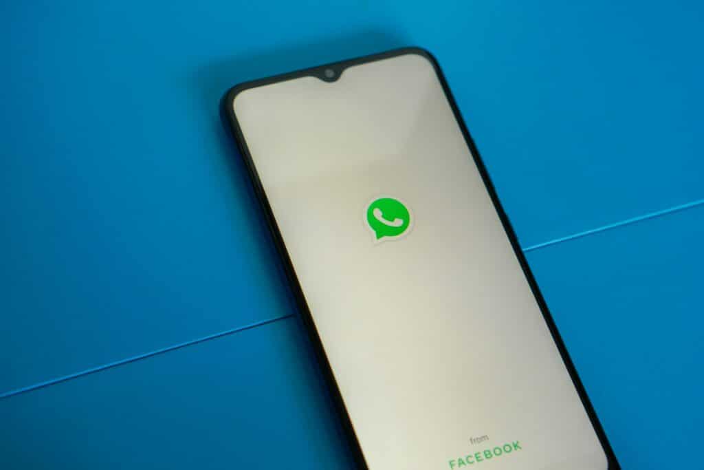 Celular apoiado sobre uma superfície plana e azul, com a tela ligada na página de carregamento do WhatsApp, mostrando o ícone do app ao centro