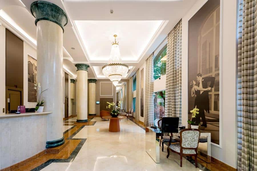 Recepção do hotel com pilastras altas de mármore, um enorme lustre no meio, algumas cadeiras e uma imagem em preto e branco na parede, ilustrando post Hotéis Mercure em São Paulo.