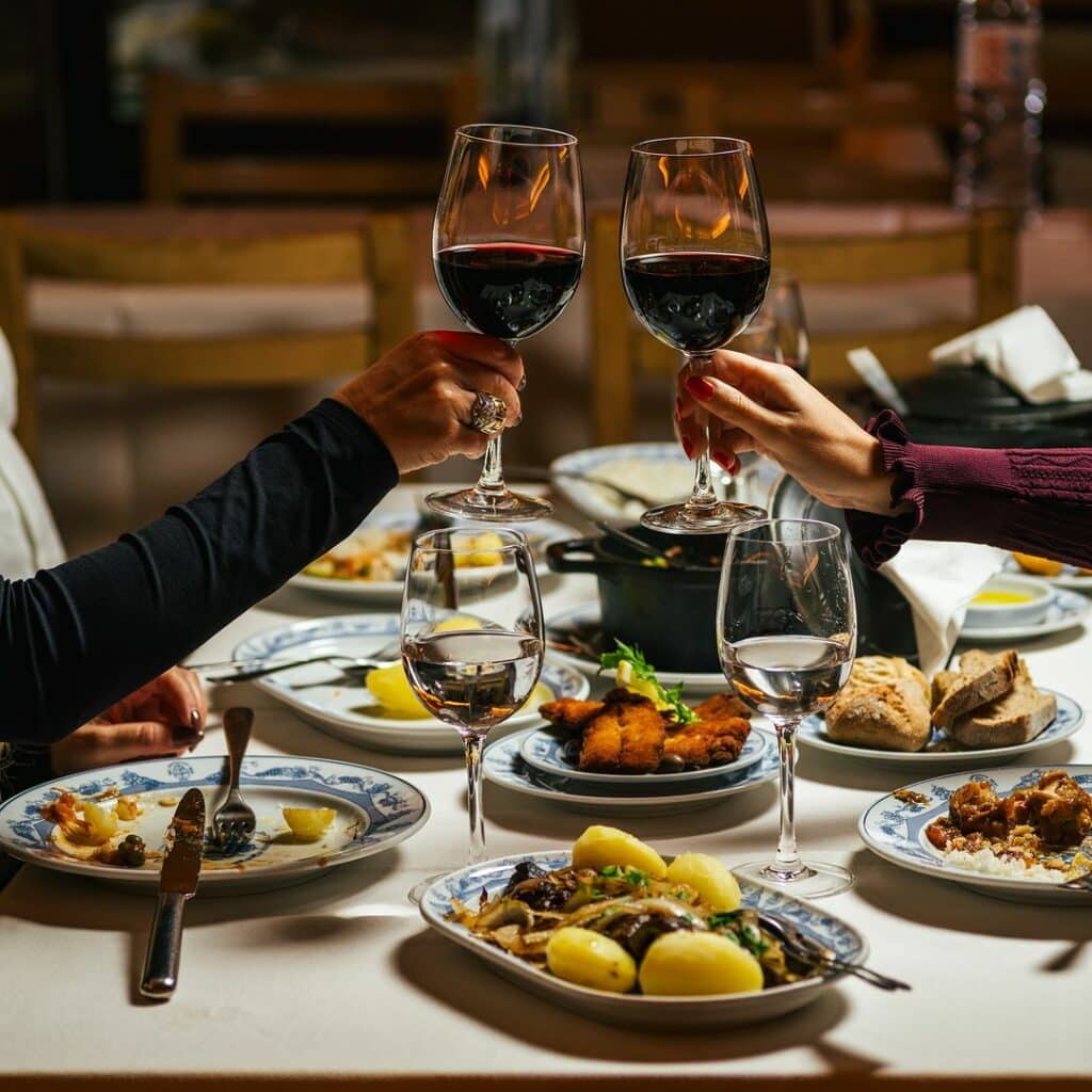 Mesa do Restaurante Adega São Nicolau com vários pratos locais na mesa com vinho e duas pessoas brindando. Representa Porto.