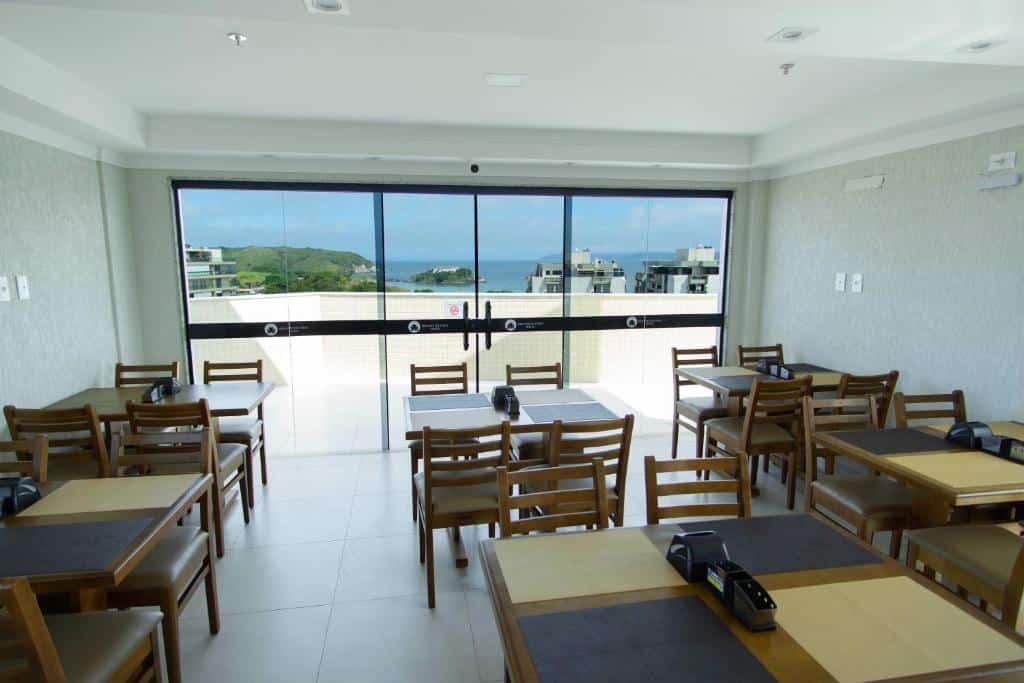 Saguão de um hotel com mesas e cadeiras para café da manhã com varanda de frente para o mar.