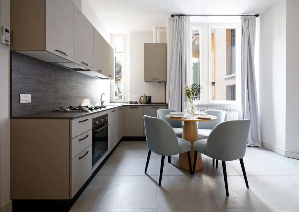 Cozinha do numa I Loreto Apartments com uma janela com cortinas, uma pequena mesa com quatro cadeiras estofadas, e uma cozinha com fogão, forno, móveis e pia