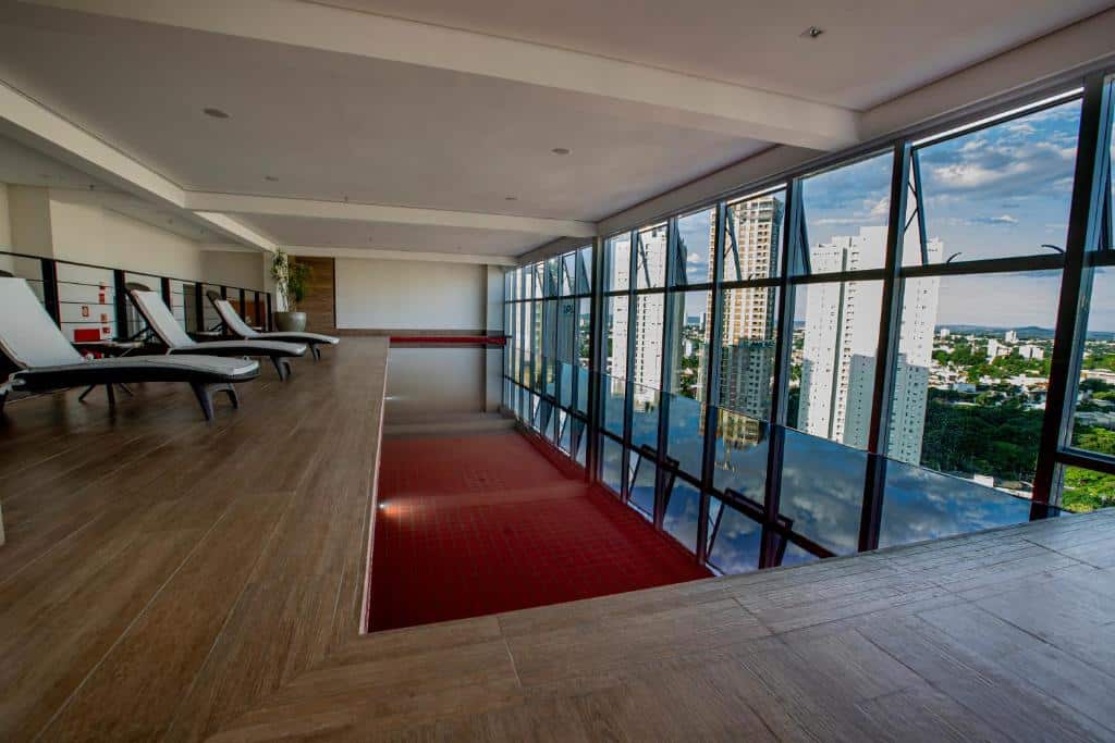 Piscina coberta em hotel com grandes janelas de vidro que dão vista para a cidade de Goiânia.