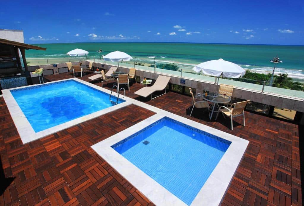 Duas piscinas quadradas, uma maior que a outra, com cadeiras ao redor, vista da piscina para o mar. Foto para ilustrar post sobre hotéis perto do Consulado Americano em Recife.